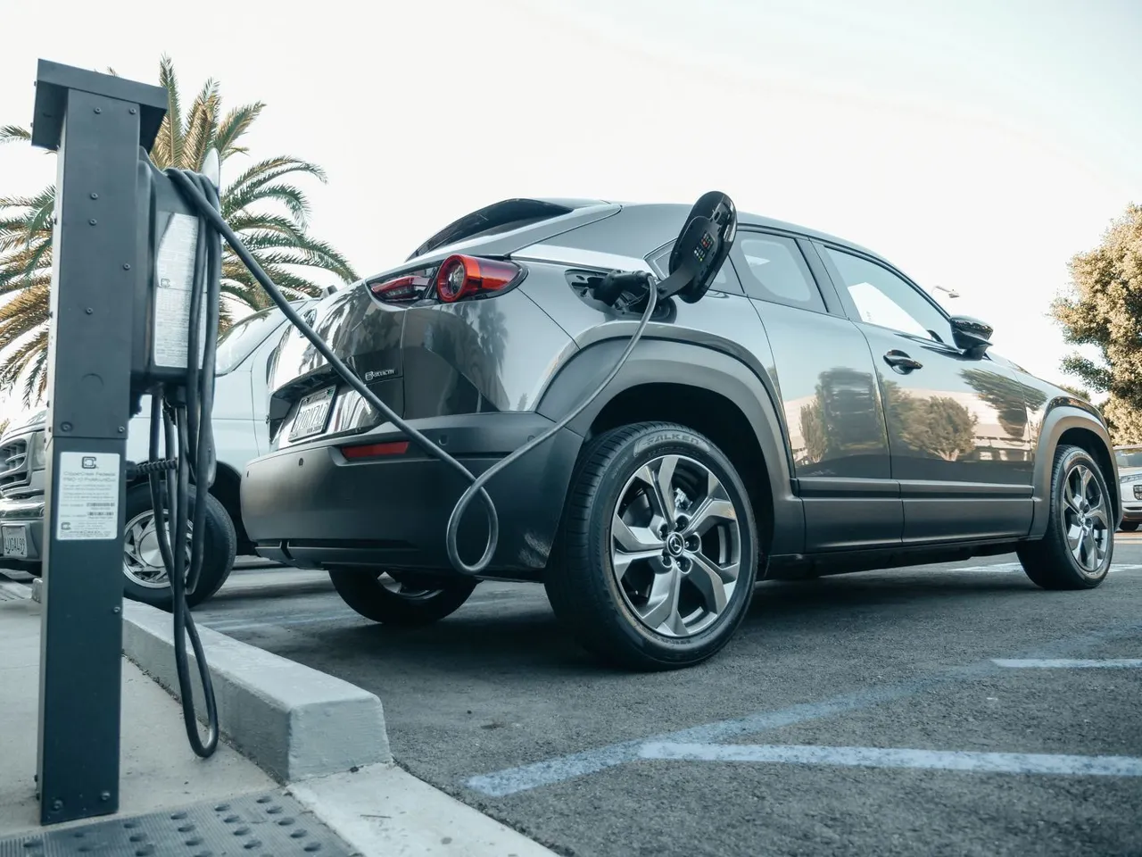 Gray electric SUV connected to a public charging station on a sunny day